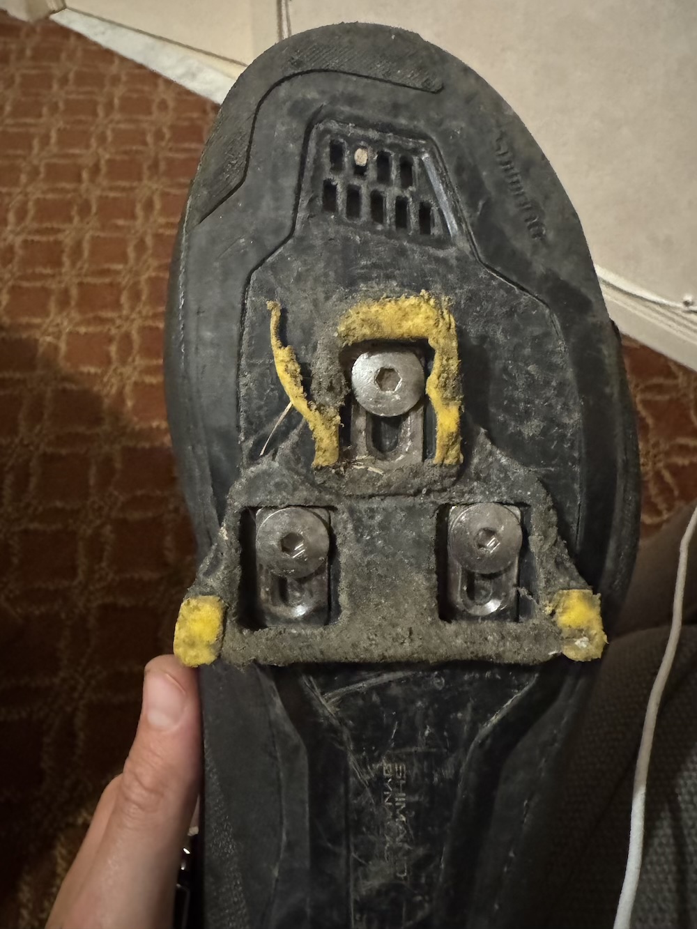 The underside of a cycling shoe, with a very worn out and broken cleat.