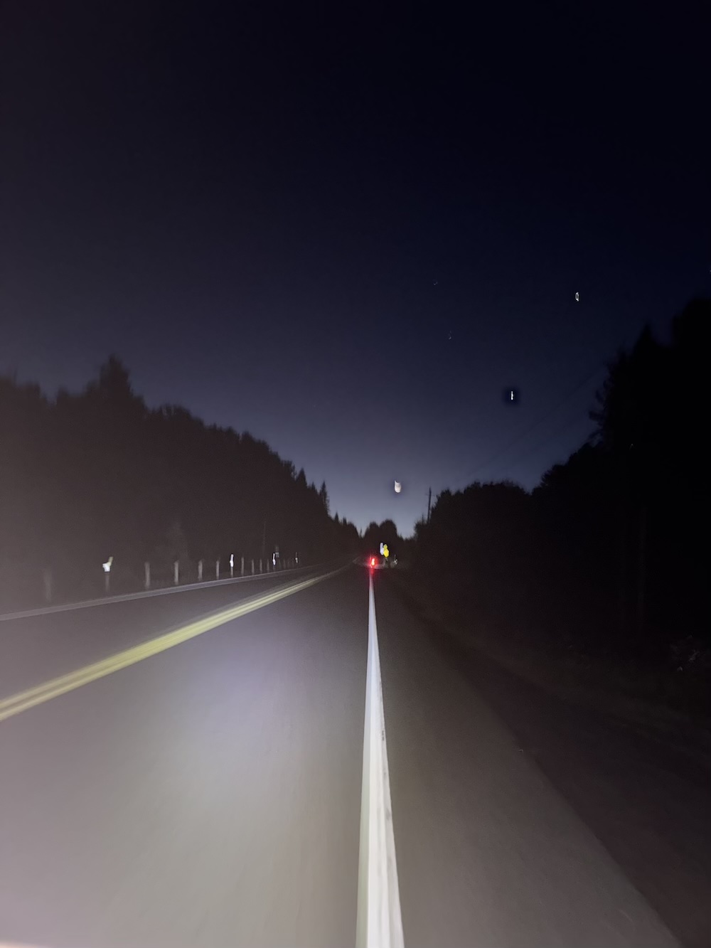 Moon and stars on the horizon of an uphill section of road.