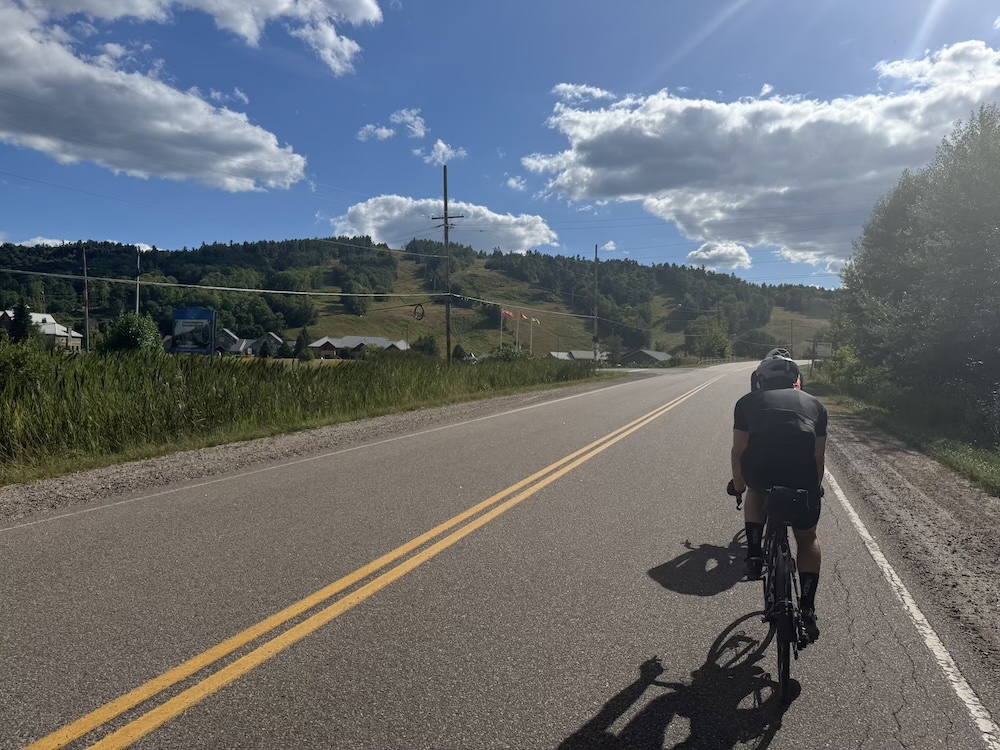 Cyclist passing a farm on a ridge along the Canadian shield.