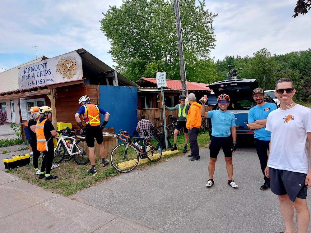 A group of cyclists in front of a shop and a support vehicle.